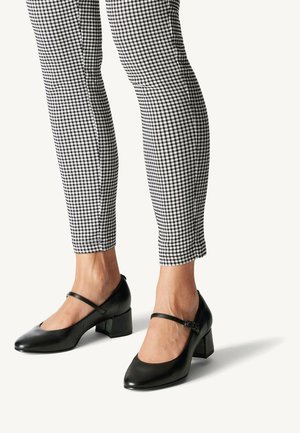 Scarpe nere in pelle con tacco a blocco, punta affilata e cinturino alla caviglia, abbinate a pantaloni attillati in fantasia scozzese bianco e nero.