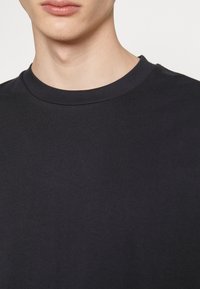 Tricou negru din bumbac cu guler rotund, având o textură netedă și un design ajustat, potrivit pentru îmbrăcăminte casual.