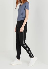 Grijze V-hals T-shirt gecombineerd met zwarte taps toelopende joggers met zijstrepen en zakken, gedragen met witte sportieve sneakers.