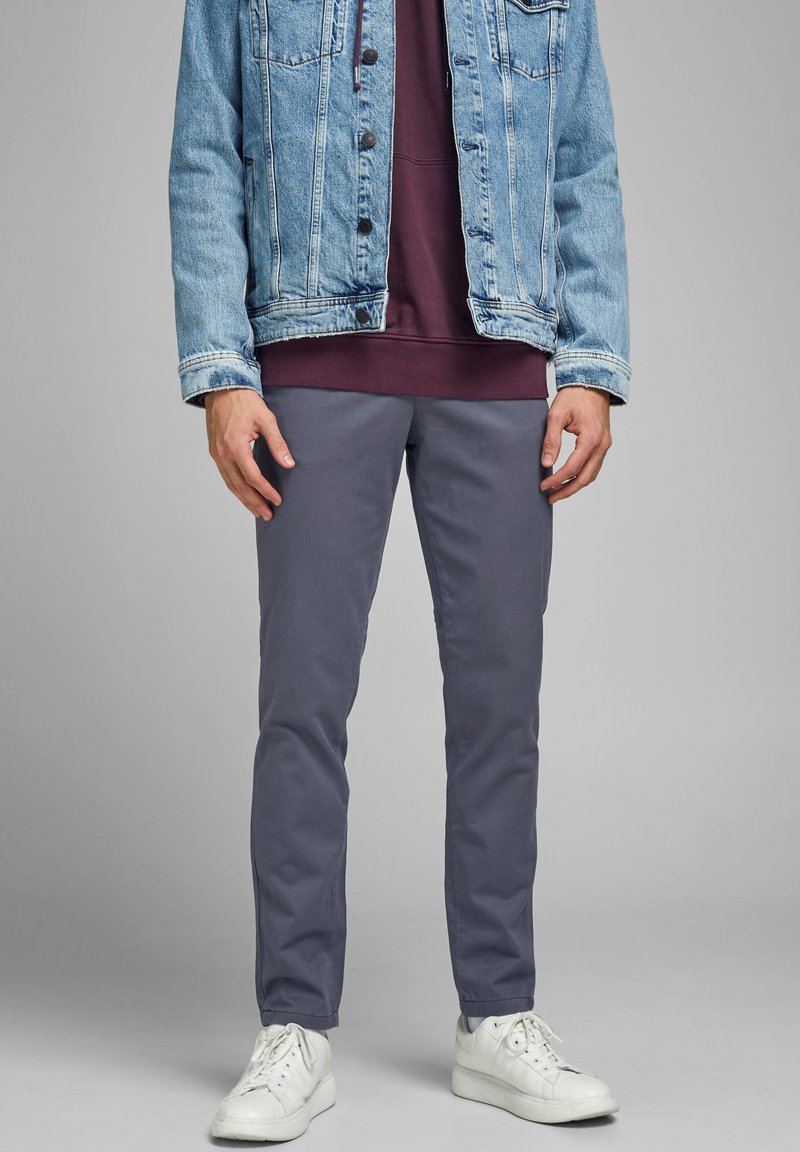 Chaqueta de mezclilla azul claro sobre una sudadera Burdeos, combinada con pantalones grises y zapatillas blancas. El conjunto presenta un diseño casual y en capas.