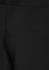 Černé kalhoty s hladkou texturou, minimalistickým designem a malou zadní kapsou s skrytým švem.