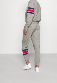 Grå sweatshirt och matchande joggers med blå och röda ränder på ärmarna och byxbenen. Har ribbade mudd och nederkant. Vita sneakers.