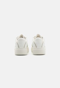 Sneakers bianchi in pelle con finitura testurizzata, con accenti beige, una suola spessa e logo in rilievo sul tallone.