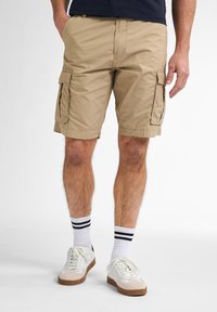 Khaki cargoshorts met een gladde textuur, zijzakken en een gestikte zoom. Gepaard met witte sneakers en gestreepte sokken.