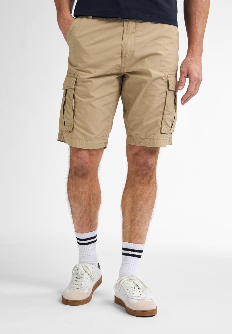 Khaki cargoshorts met een gladde textuur, zijzakken en een gestikte zoom. Gepaard met witte sneakers en gestreepte sokken.