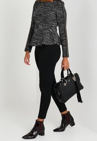 Top peplum testurizzato bianco e nero, leggings neri, stivaletti bordeaux lucidi alla caviglia e una borsa nera con dettaglio a frange e accessori in argento.