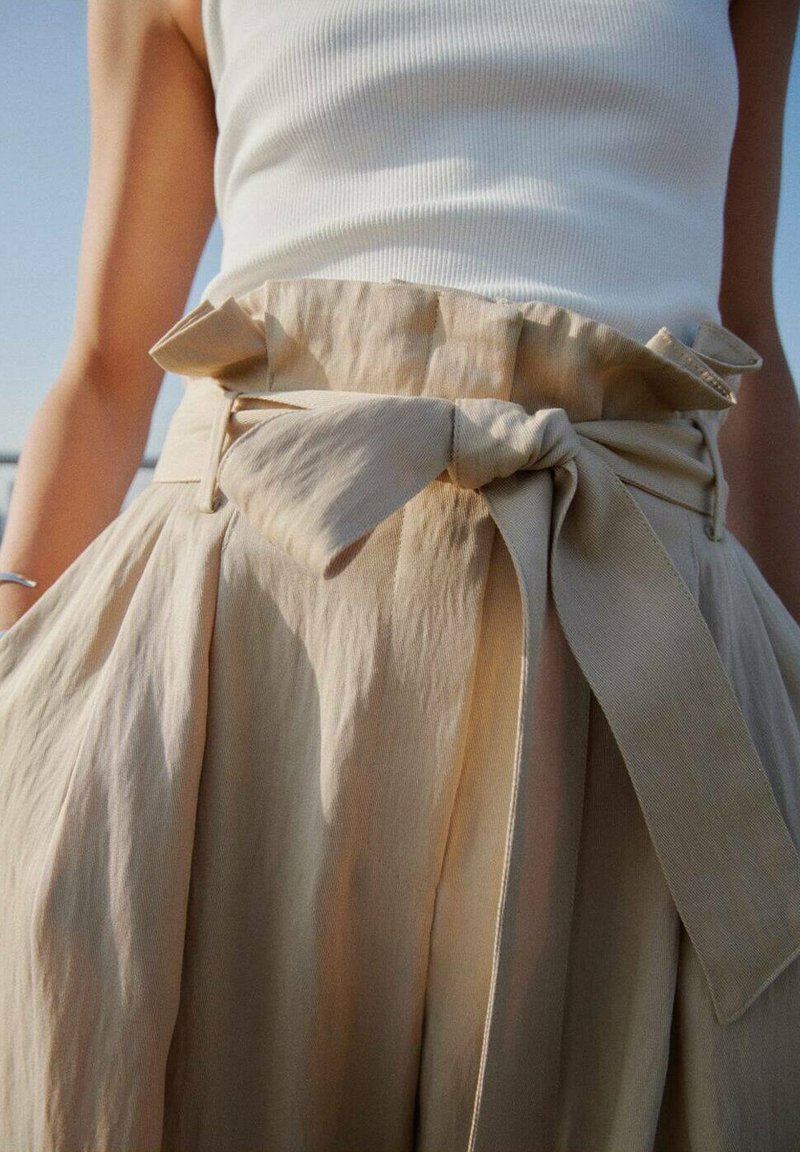 Jupe beige taille haute avec une taille élastique froncée, détail de nœud lié et un design plissé en tissu léger.