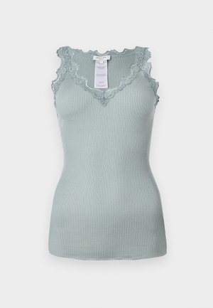 Top de tirantes de color verde claro con textura acanalada, cuenta con un escote y tirantes adornados con puntilla en forma de concha. La tela es elástica y de textura suave. Etiqueta visible en el interior.