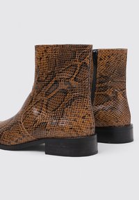 Bottes ankle imprimé serpent marron avec une texture lisse, bout rond et une accent de fermeture éclair noire sur le côté ; talon bloc bas.