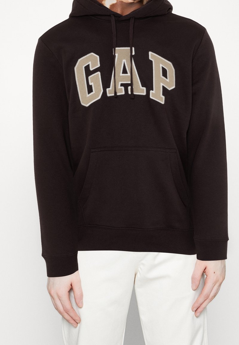 Felpa nera con tasca a marsupio, caratterizzata da un grande logo "GAP" color beige. Presenta lacci e polsini a coste sulle maniche.