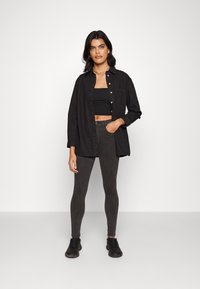 Camisa preta oversized com botões, top cropped preto, jeans skinny escuros e ténis pretos. Tecido suave e design ajustado.