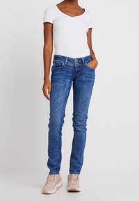 Blå denim jeans med smal passform, med knappstängning, femficksdesign och lätt utslitet utseende. Matchas med en vit ribbad topp.