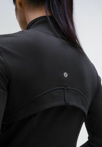 Pull noir de sport à col montant, avec un design à coutures plates et un petit logo de marque au dos. Texture de tissu lisse et ajusté.