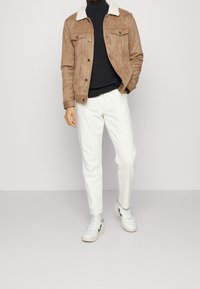 Brun mockaskinnjacka med vit skinnfårskinnskrage, svart polotröja, vita byxor och vita sneakers med svarta detaljer. Avslappnat outfit.