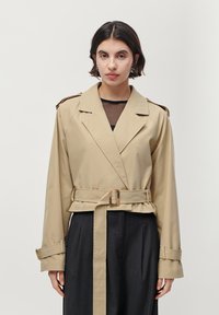 Beige trenchcoat met een wikkelontwerp, brede revers, een ceintuur in de taille en lange mouwen. Bevat schouderepauletten en een gladde textuur.