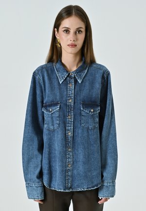 Dunkelblaue Jeanshemd mit spitzem Kragen, zwei Brusttaschen und einer Knopfleiste. Lange Ärmel mit umgeschlagenen Säumen.
