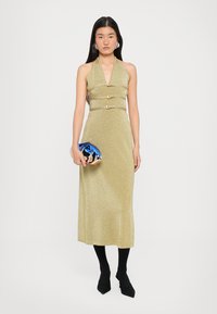 Shimmery gold halter dress with fitted bodice and two silver buckle accents. Accompanied by a blue clutch and black tights with pointed shoes.