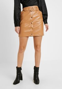 Ruskea keinonahkainen hame, jossa on etupainike ja vyö pyöreällä soljella. Teksturoitu pinta ja slim fit -muotoilu. Mustat nilkkasaappaat.
