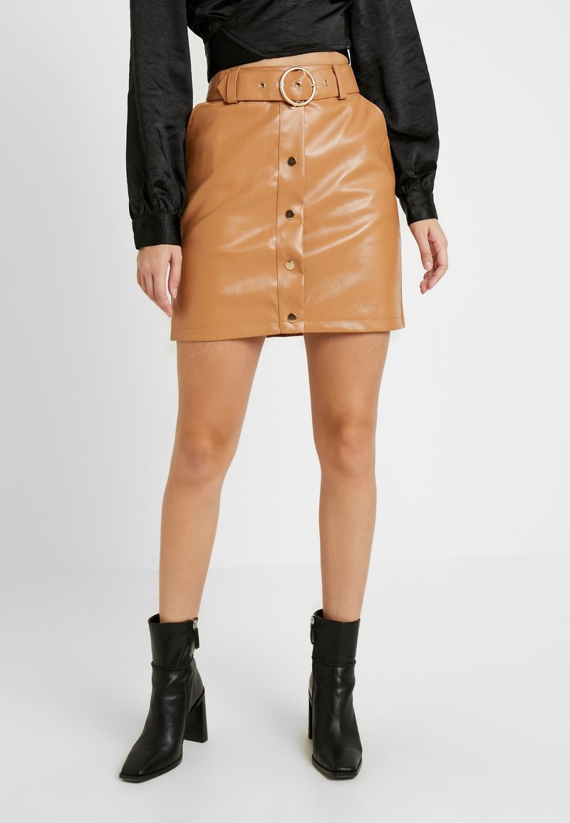 Ruskea keinonahkainen hame, jossa on etupainike ja vyö pyöreällä soljella. Teksturoitu pinta ja slim fit -muotoilu. Mustat nilkkasaappaat.