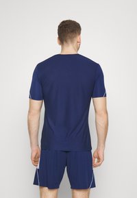 Camiseta deportiva en azul marino con mangas cortas, que presenta un patrón de malla texturizada. Tiene acentos en blanco contrastantes en las mangas.