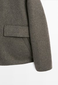 Cappotto di lana grigio con design su misura, rever a punta, tasca a patta e una finitura morbida e testurizzata.