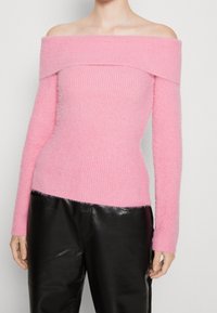 Różowy sweter o fasonie off-the-shoulder, wykonany z miękkiego prążkowanego materiału, z długimi rękawami. Połączony z błyszczącymi czarnymi skórzanymi spodniami.