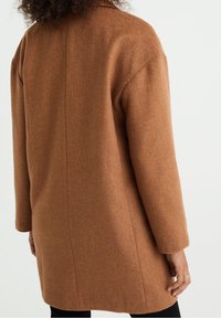 Brązowy płaszcz z mieszanki wełny o prostym kroju, długich rękawach i kołnierzu z wcięciem. Charakteryzuje się gładką fakturą i minimalistycznym designem.