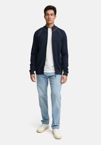 Granatowy sweter zapinany na zamek z teksturowanej tkaniny z prążkowanymi mankietami, zestawiony z jasnoniebieskimi dżinsami i białymi trampkami. Minimalistyczny design, bez wzorów.