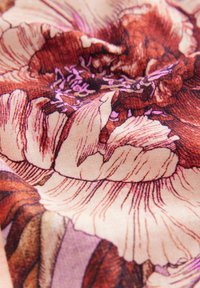 Material floral cu flori mari de culoare roșu-maro și accente violet pe un fundal deschis, prezentând texturi și linii detaliate.