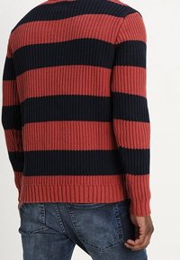 Knit sweater with horizontal red and navy stripes, ribbed texture, and a crew neck. Long sleeves and a finished hem at the waist.