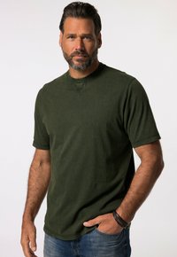 Camiseta de manga corta verde oscuro, hecha de un tejido suave y texturizado, con cuello redondo y sutiles detalles de costura, llevada con jeans azules.