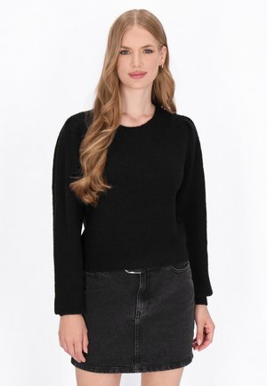 Schwarzer gestrickter Pullover mit langen Ärmeln und rundem Halsausschnitt, kombiniert mit einem enganliegenden schwarzen Jeansrock. Strukturiertes Material, schlichtes Design.