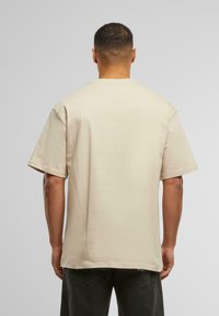 Beige oversized t-shirt with short sleeves, round neckline, and a smooth texture, displayed from the back against a light gray background.