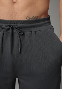 Donkergrijze joggers van een gestructureerde stof, met een elastische tailleband, verstelbare koord en zijzakken. Heeft een nauwsluitend ontwerp.