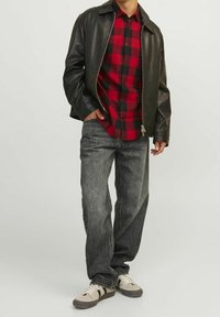 Chaqueta de cuero negra sobre una camisa de cuadros en rojo y negro, combinada con jeans grises y zapatillas gris claro con acentos oscuros.