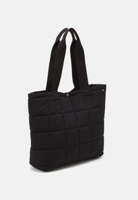 Mustat peitoiset kantokassi, jossa on pehmeä rakenne, kahdella mustalla kangaskahvalla ja messinkisestä napista suljettava. Pintakuvio neliöinä.