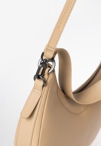 Beige leren tas met een gebogen silhouet, platte schouderriem en metalen accessoires met een druksluiting. Gladde textuur met zichtbare stiksels.