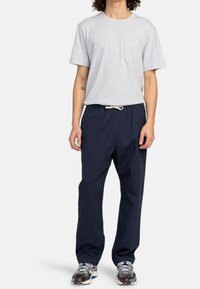 T-shirt gris en coton avec une poche poitrine, associé à un pantalon bleu marine à cordon. Le modèle porte des baskets noires et grises. Coupe décontractée avec un design relax.