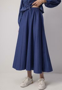 Gonna blu, lunga fino alla caviglia, con vita elastica, realizzata in tessuto morbido; presenta un design ampio e svasato ed è abbinata a sneakers bianche.