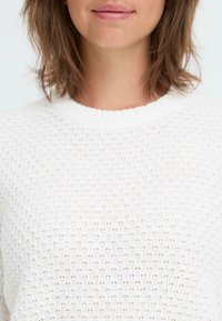 White knitted sweater with a textured pattern and a ribbed neckline, featuring a loose fit and breathable fabric.