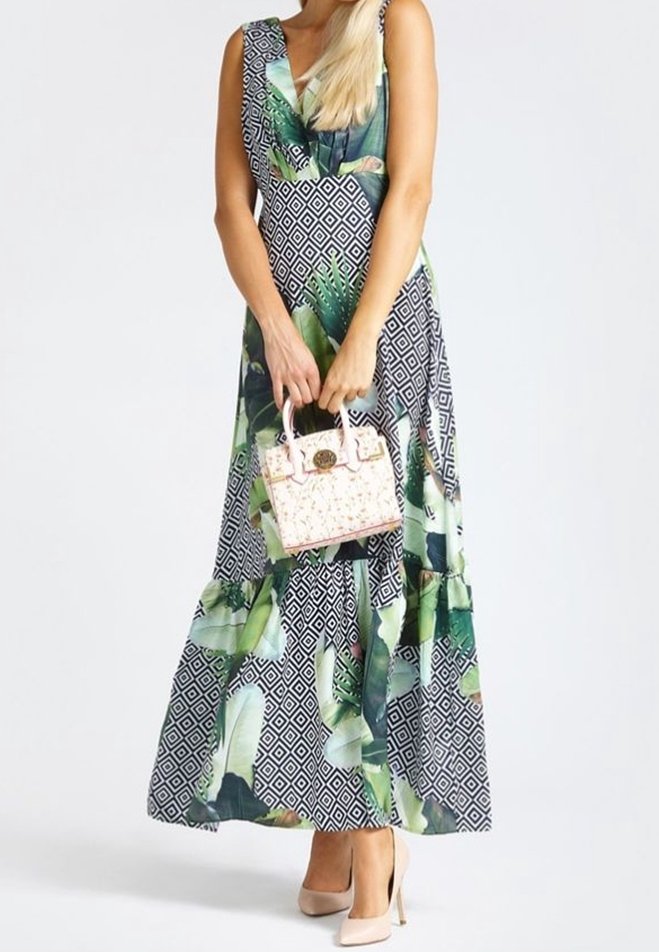 Maxi-jurk met een marineblauw en groen bladmotief, voorzien van geometrische patronen. Draagt een lichtroze handtas en nude hoge hakken.