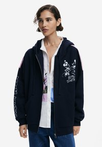 Dunkelblaue Zip-Front Kapuzenjacke mit rosa Akzenten, Grafik von Mickey und Minnie Mouse und dem Text "Besser Zusammen" auf der Vorderseite. Baumwollmischgewebe.