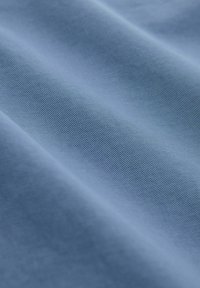 Tissu bleu lisse avec une fine texture nervurée diagonale et des ombres douces mettant en valeur des plis délicats.