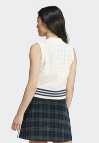 Top sem mangas em malha creme com colarinho canelado e faixa azul-marinho na barra, combinado com uma saia xadrez verde-escura.