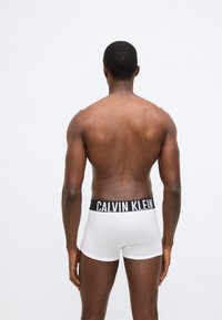 Λευκά ανδρικά εσώρουχα boxer με μαύρη ζώνη μέσης CALVIN KLEIN, κατασκευασμένα από μαλακό βαμβακερό μείγμα και εφαρμοστή γραμμή, εμφανιζόμενα από πίσω.