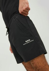 Schwarze Shorts aus leichtem Stoff mit einem elastischen Bund, ausgestattet mit einer Kordel und seitlichen Taschen. "R.D.D. Royal Denim Division"-Logo in Weiß aufgedruckt.