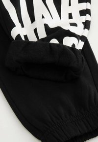 Czarne dresowe spodnie z mankietami, z wyraźnym białym graficznym napisem na górnej części oraz miękką teksturą.