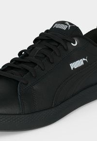 Μαύρο αθλητικό παπούτσι Puma με κορδόνια, υφασμένο πάτο και λευκό λογότυπο Puma στο πλάι και στη γλώσσα, σε απλό φόντο.