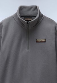 Sudadera de felpa gris con un alto cuello, que cuenta con un cierre de cuarto y un parche de logotipo de la marca en el pecho. Textura suave, diseño ligero.