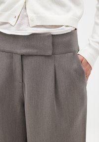 Hallid, kohandatud hallid püksid sileda tekstuuriga, ees voldid, küljetaskud ja vöökohaga detail. Paaritatud valge kardiganiga.